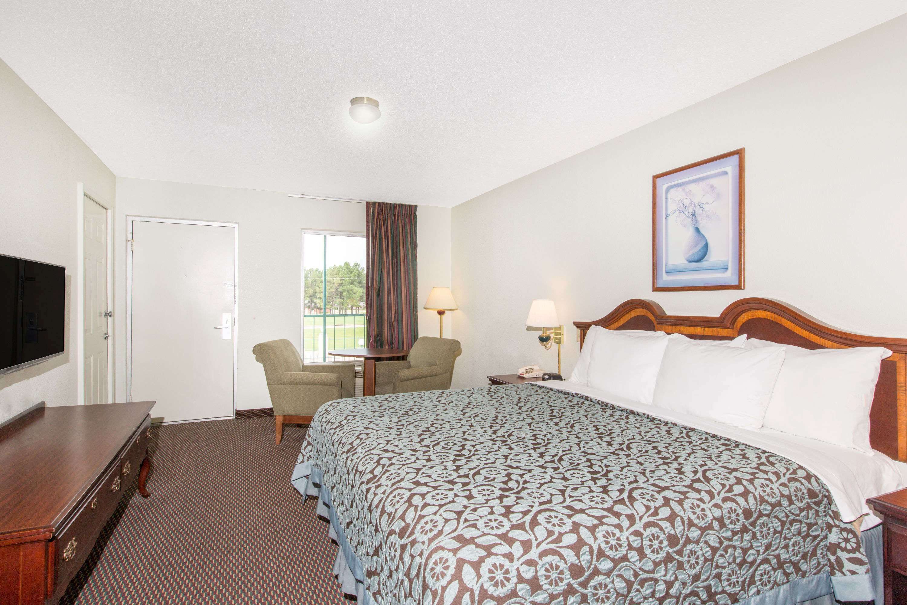 A hotel room with a bed, a desk, a chair, a TV, and a window with curtains.