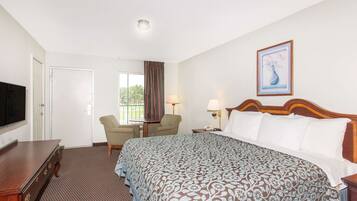 A hotel room with a bed, a desk, a chair, a TV, and a window with curtains.