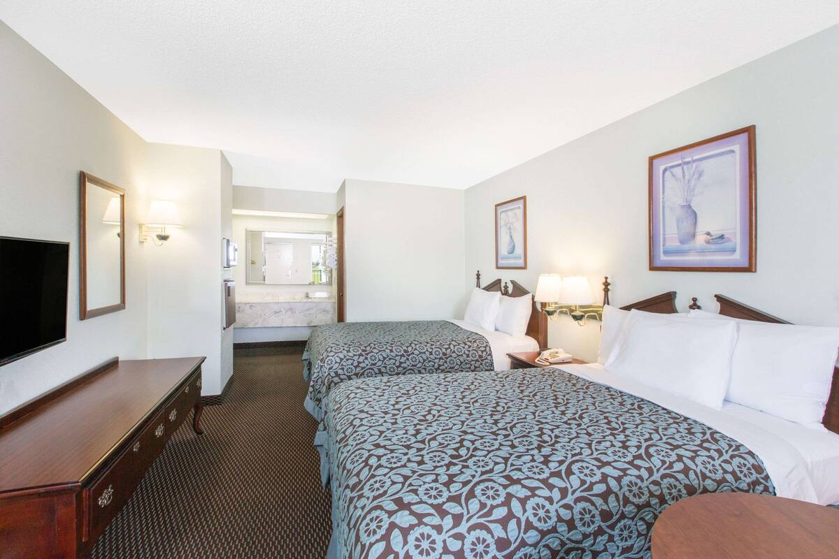 A hotel room with two beds, a TV, a dresser, and a bathroom visible in the background.