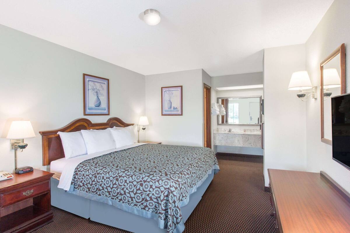 A hotel room with a bed, bedside lamps, a desk, and a mirror.