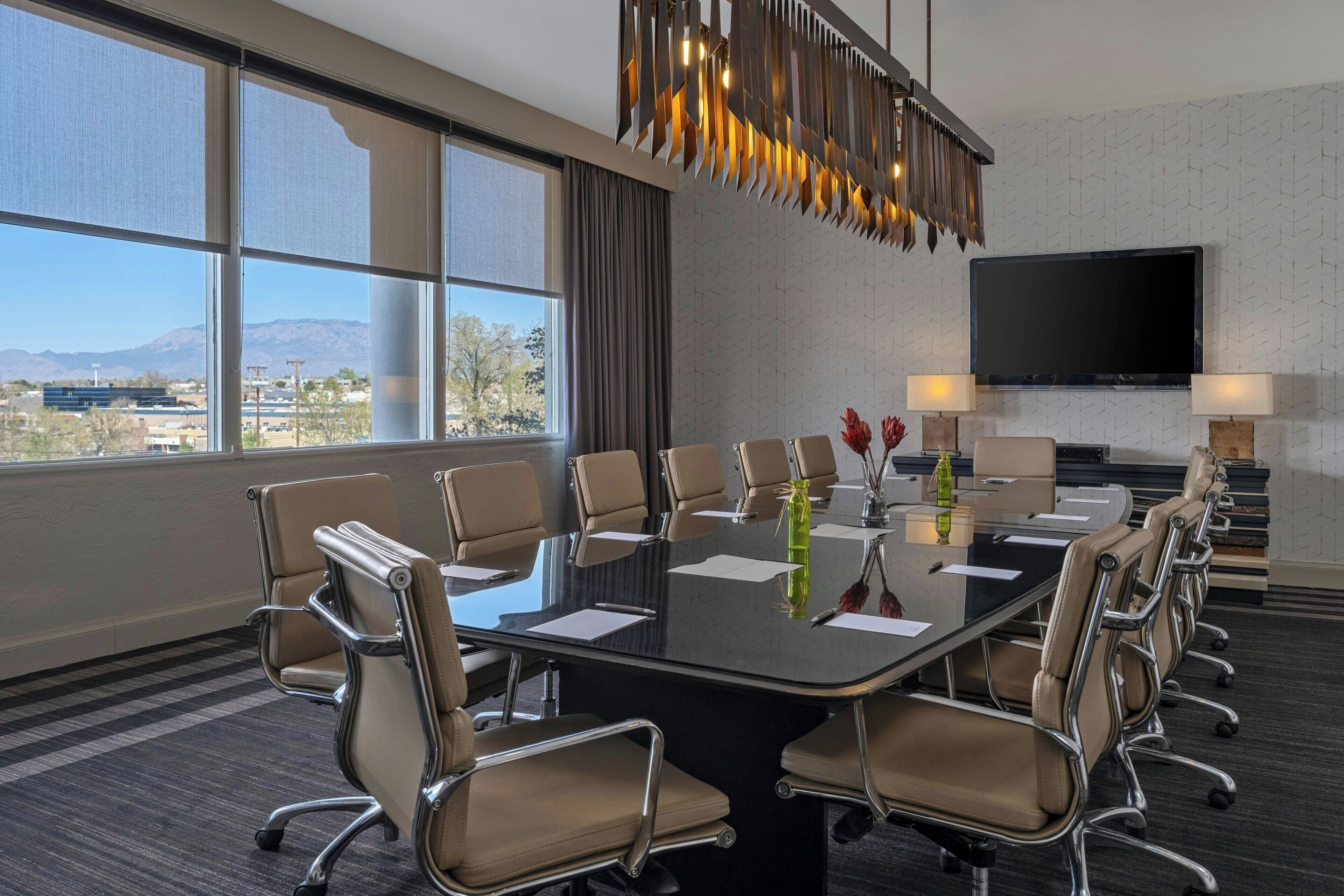 A conference room with a large table, multiple chairs, a TV, and a view of mountains.