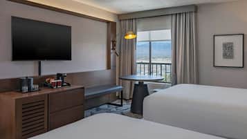 A hotel room with two beds, a TV, a desk with a coffee maker, a chair, and a table.