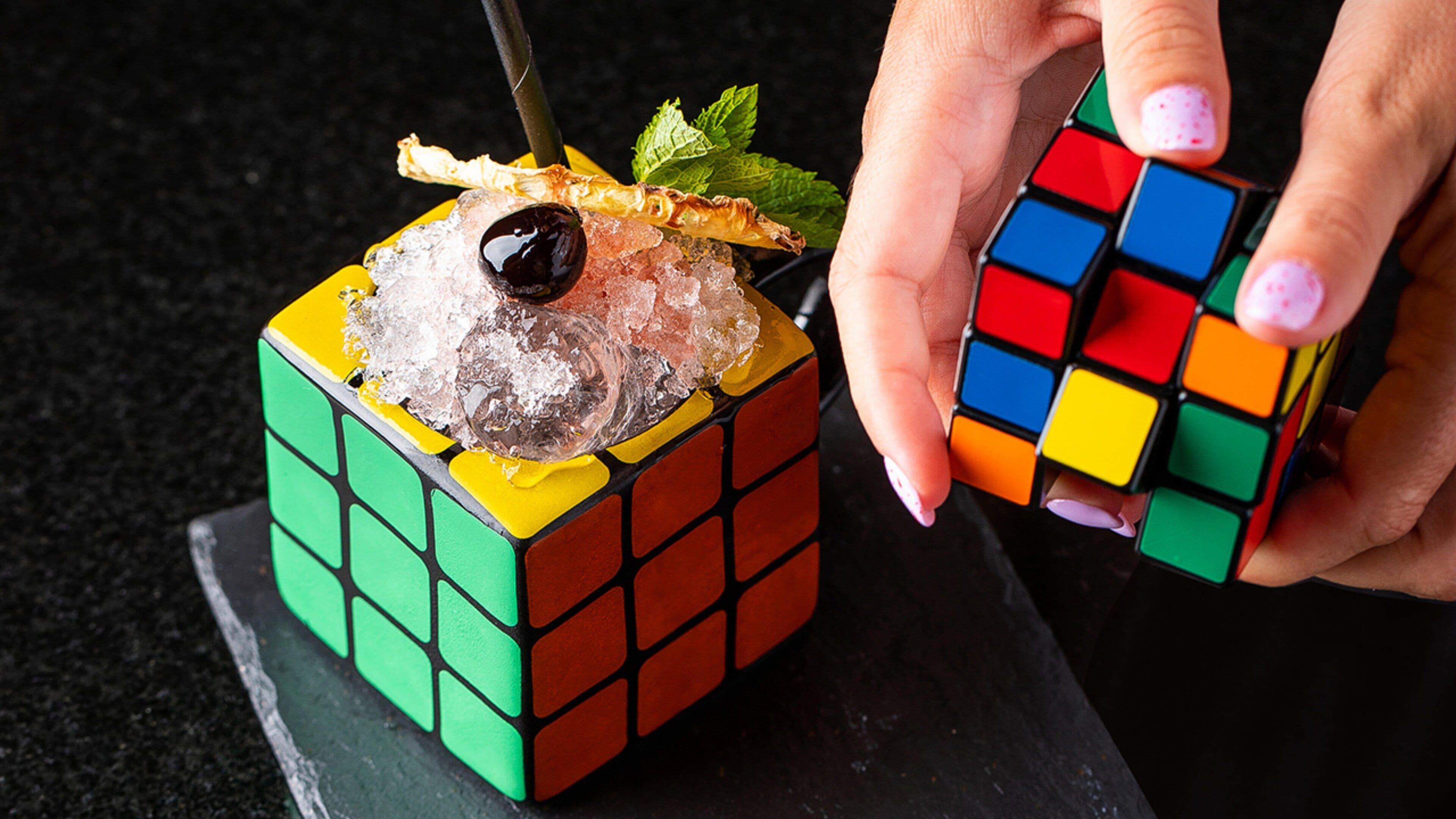 Un cubo de Rubik con una bebida colorida encima.
