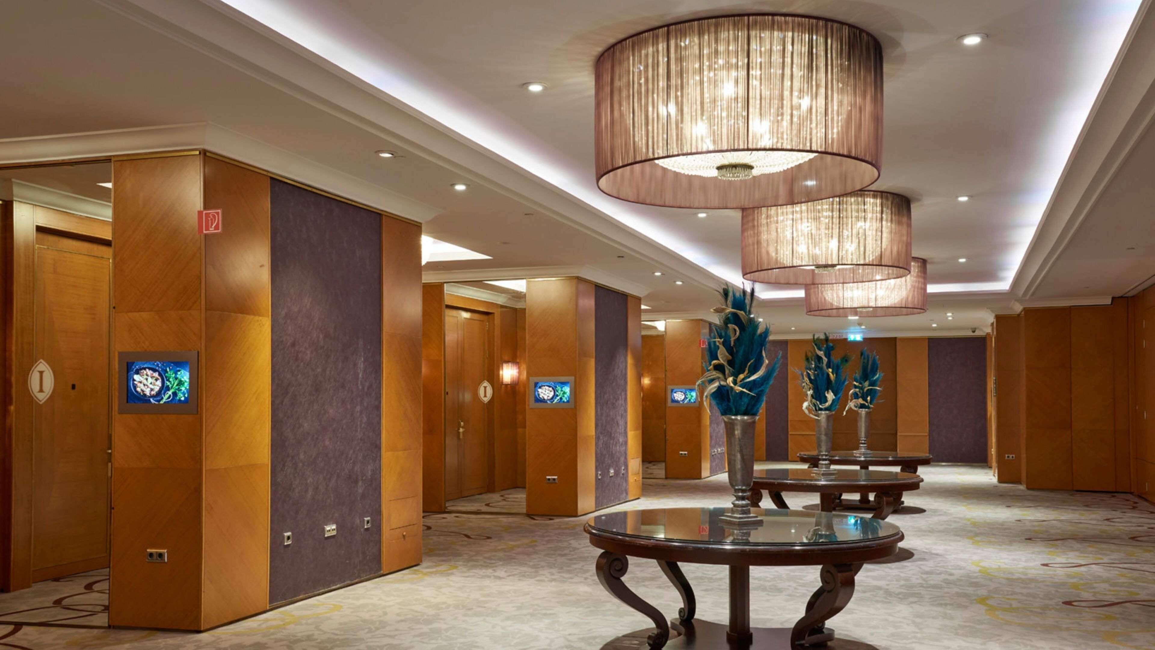 A hotel corridor with wooden paneling, a glass table, and a chandelier.
