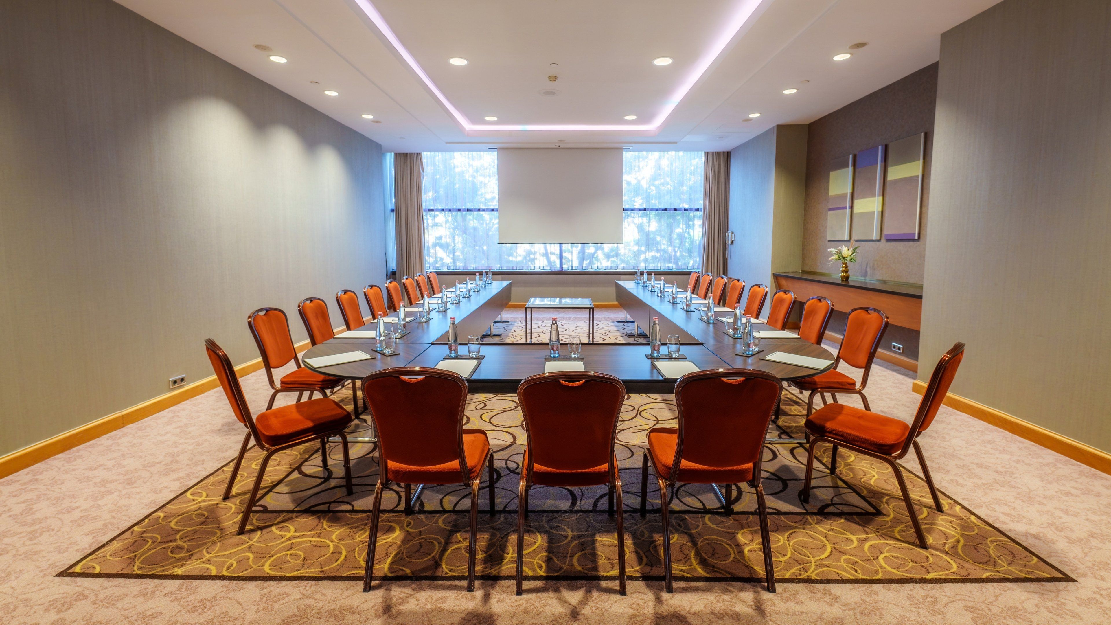 A conference room with a long table, chairs, and a projector screen.