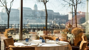 A dining table set for two with a cityscape view through large windows.
