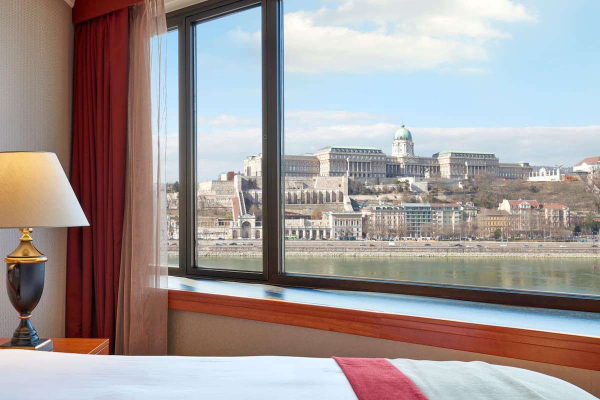 A hotel room with a large window offering a view of a historic cityscape and a river.