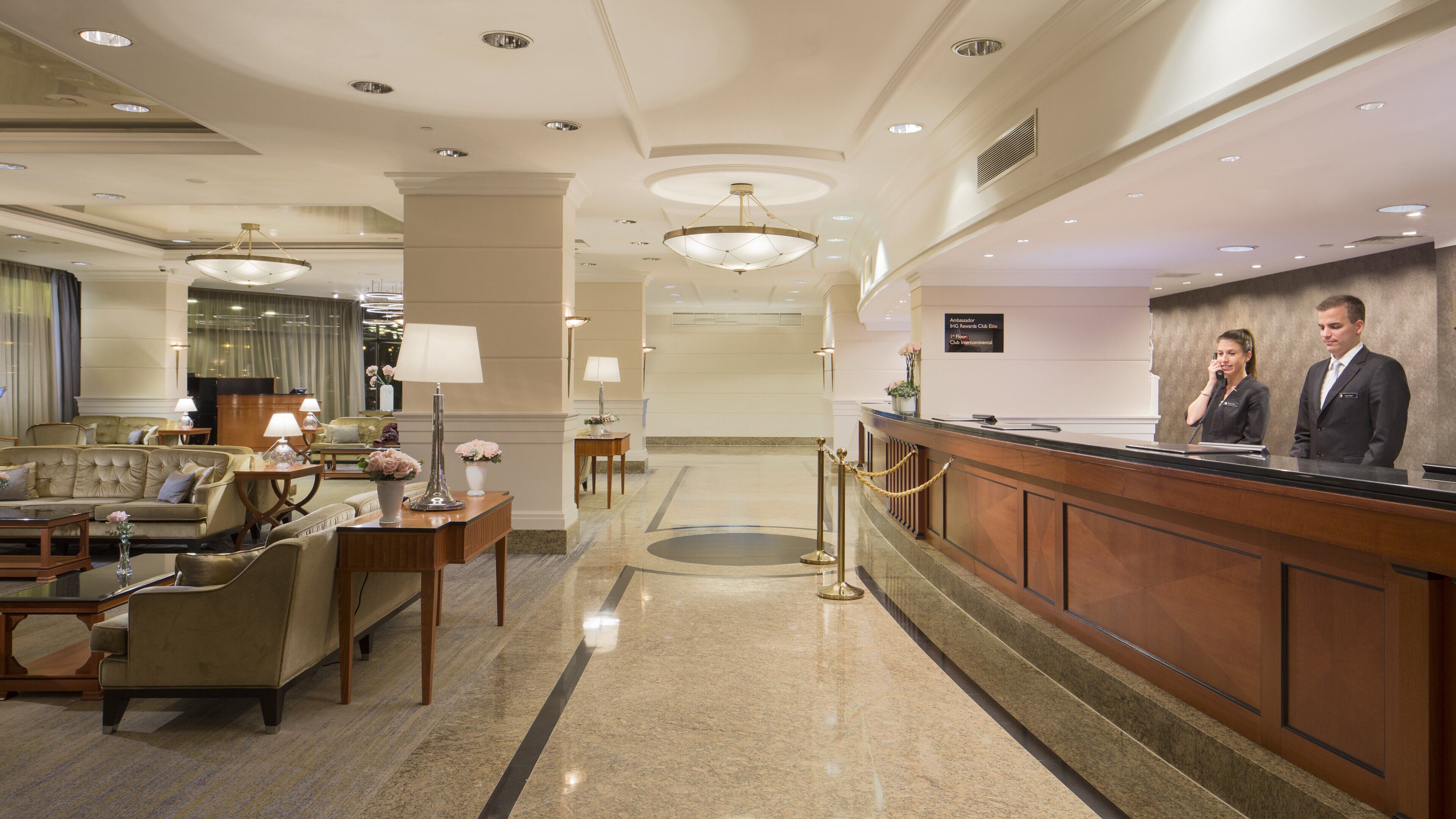 A hotel lobby with a reception desk, seating area, and a chandelier.