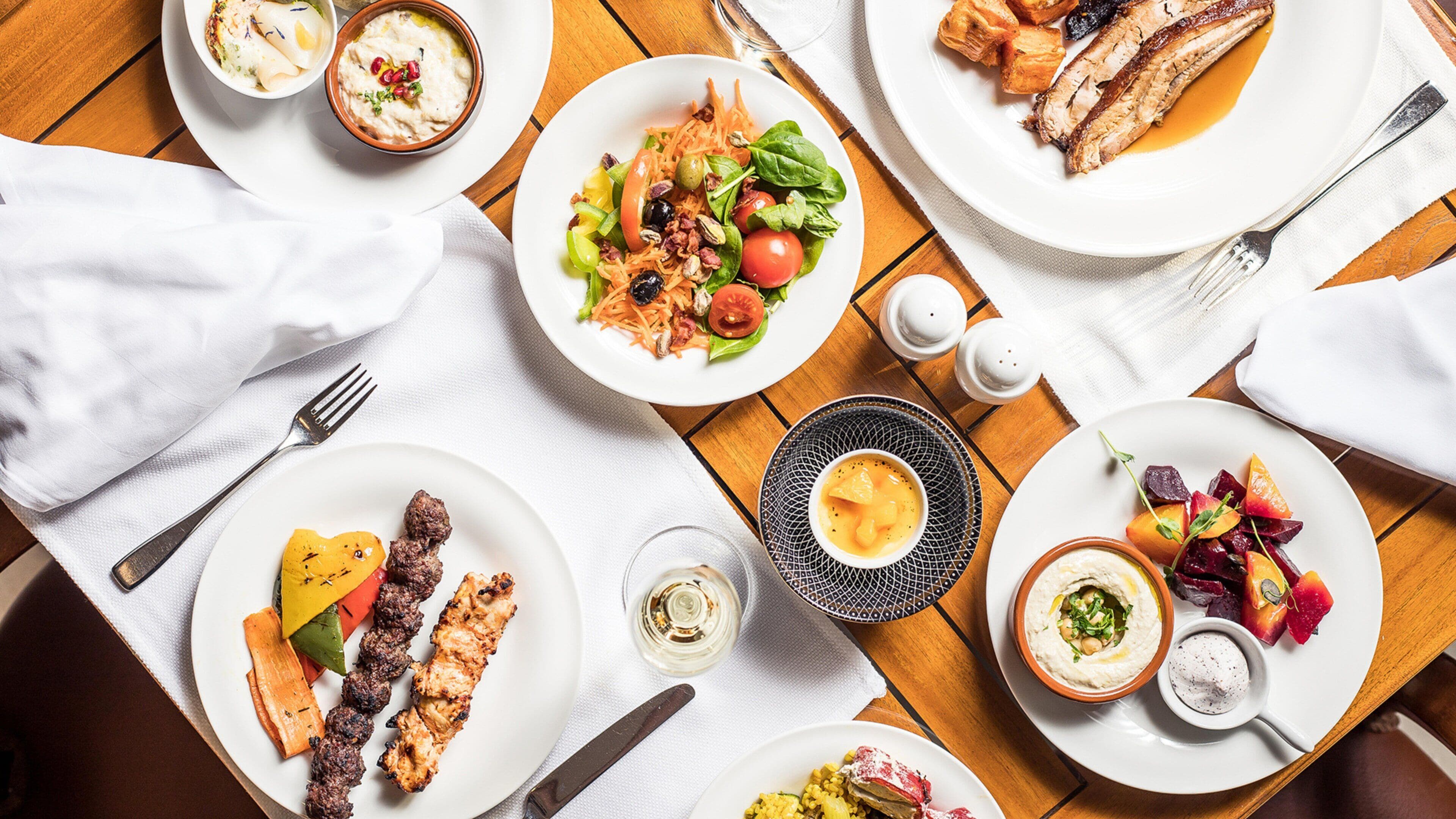 A dining table with various dishes, including grilled meat, salads, and dips.