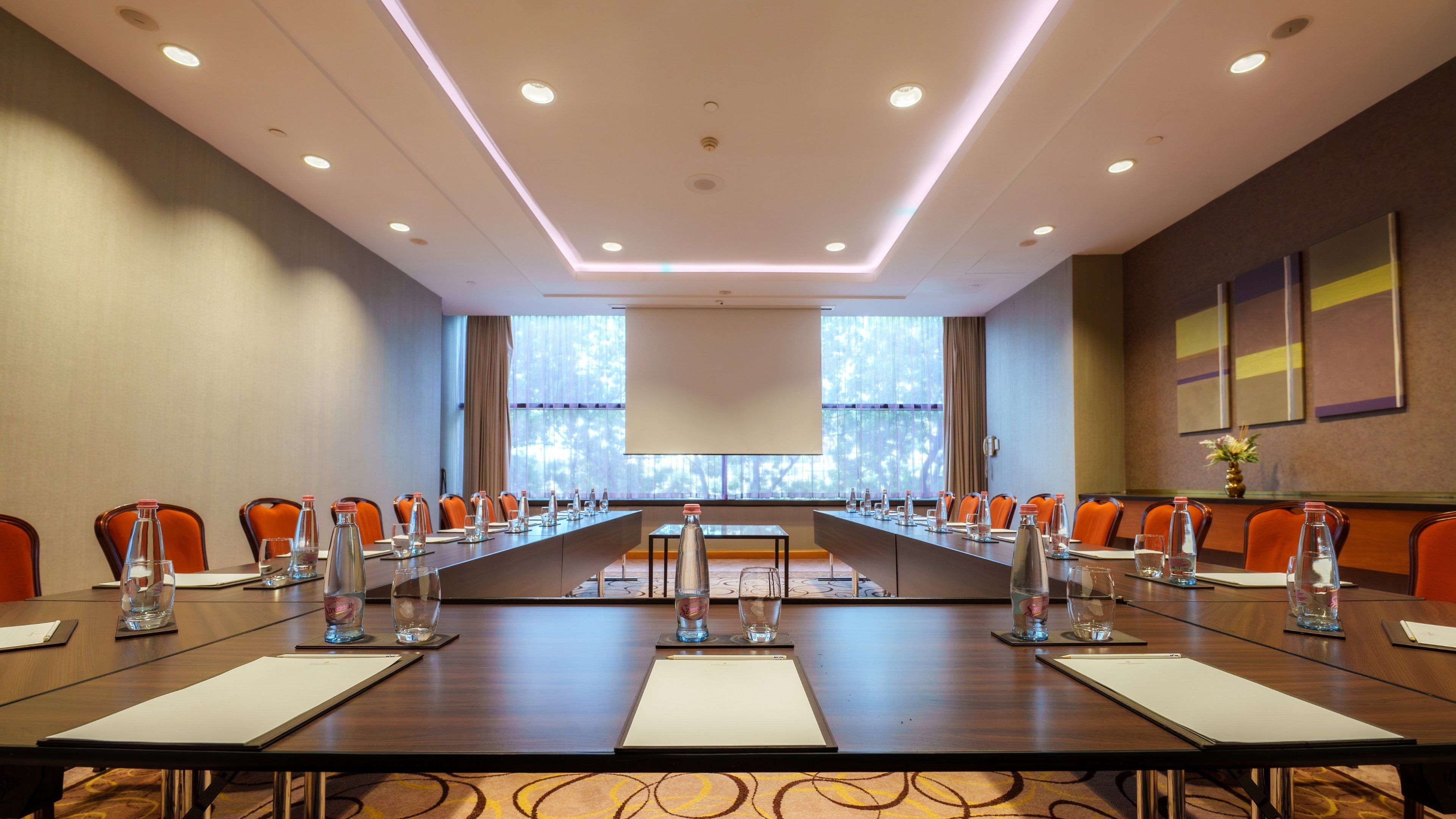 Un salón de conferencias con una larga mesa, sillas y una pantalla para proyector.