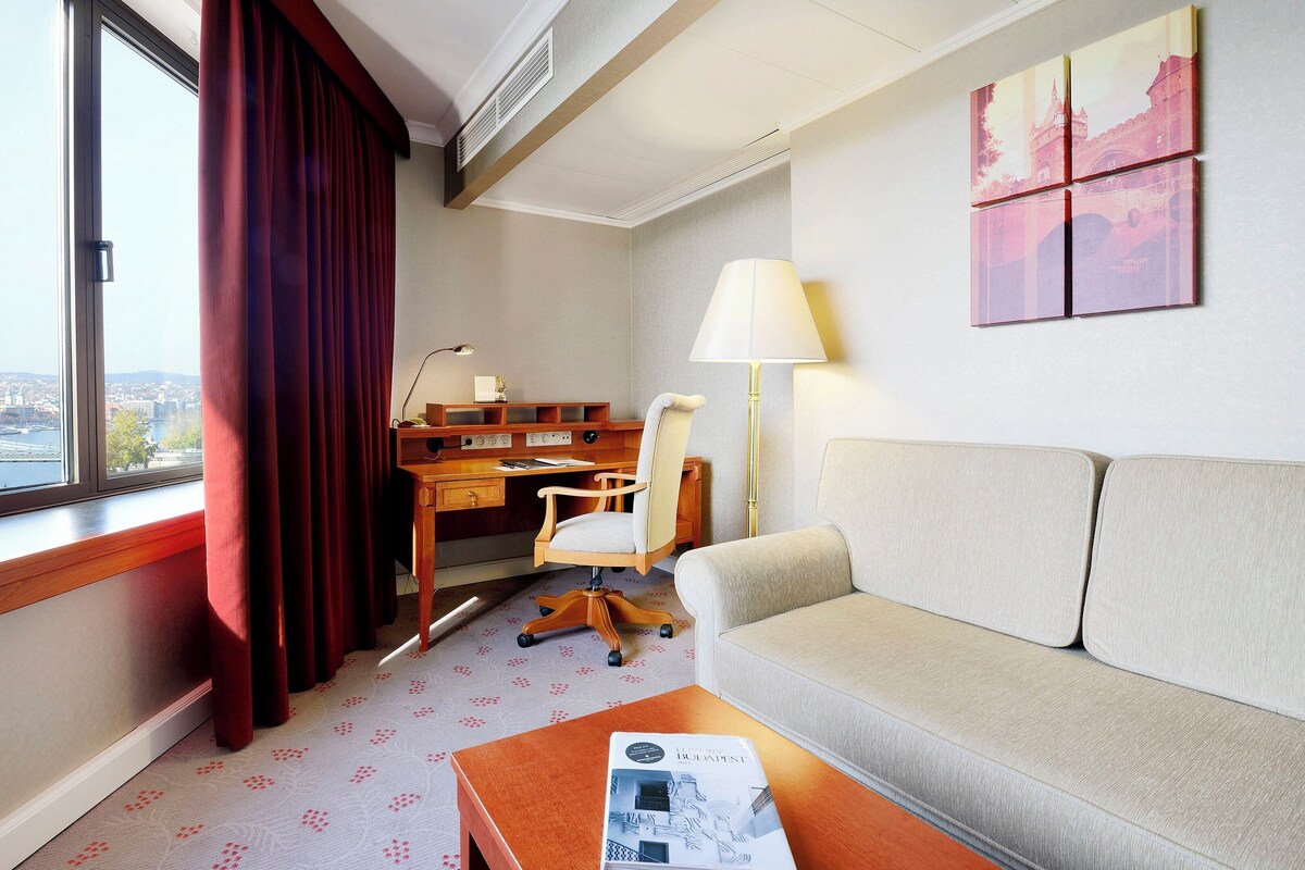 Hotellihuone, josta on näkymä sillalle, ja jossa on työpöytä, tuoli, sohva ja lamppu.