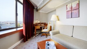 A hotel room with a view of a bridge, a desk, a chair, a sofa, and a lamp.