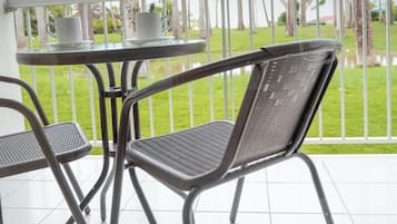 Un balcone con tavolo e due sedie, affacciato su un prato con palme.