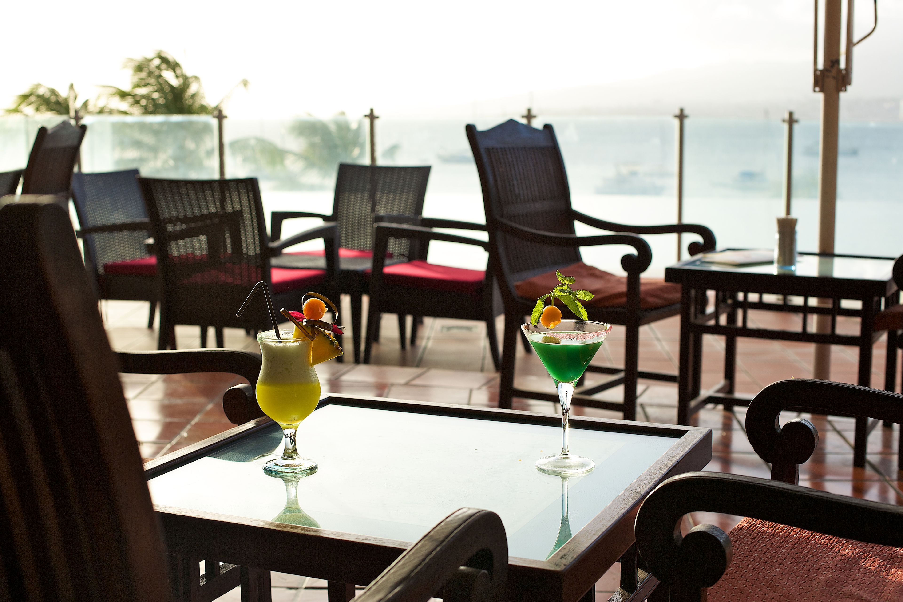 A terrace with tables and chairs, two drinks on a table, and a view of the sea.