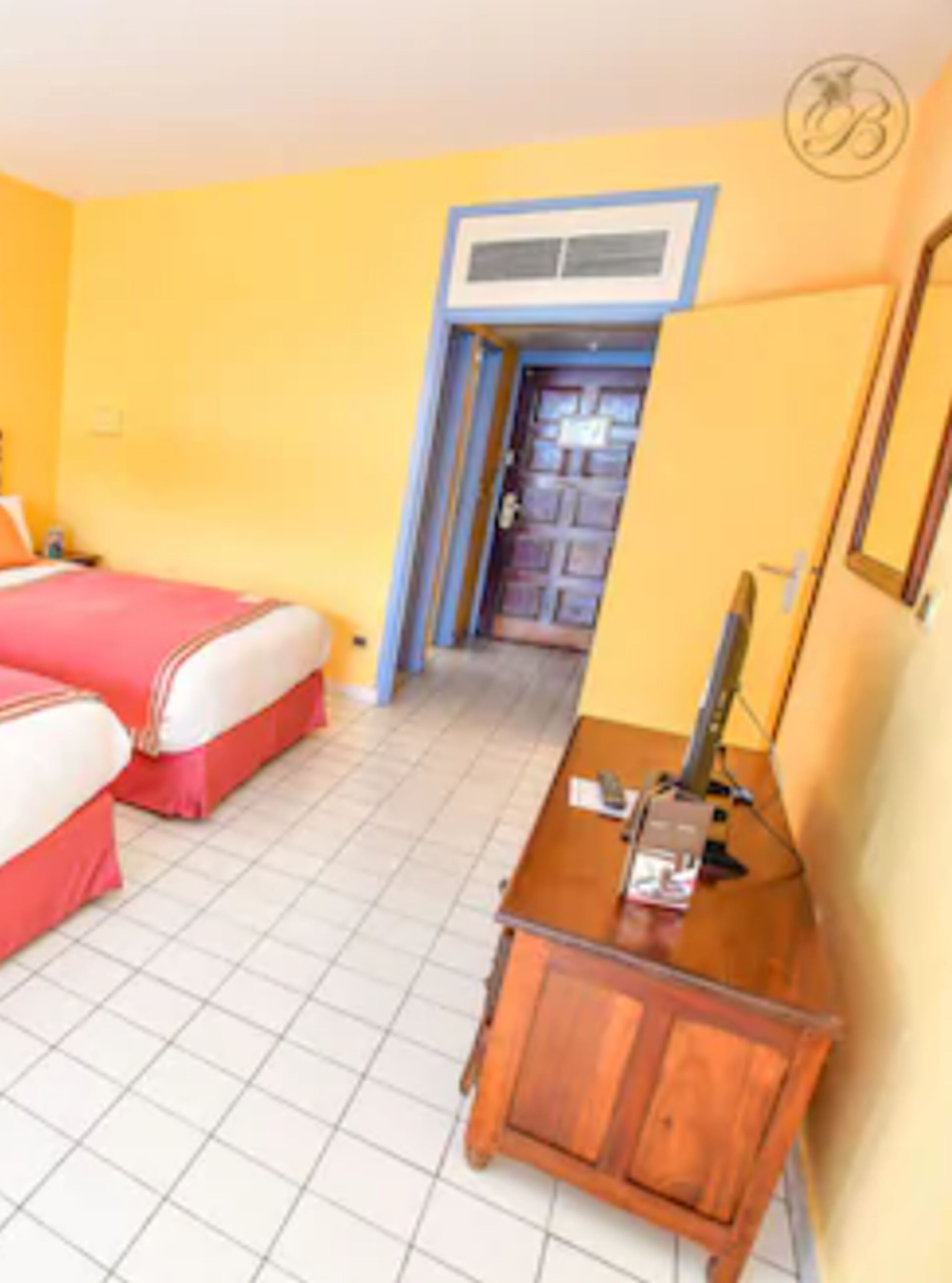 Une chambre d’hôtel avec deux lits, un bureau en bois et une porte donnant sur une autre pièce.
