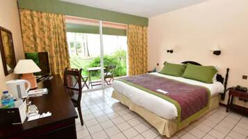 A hotel room with a bed, a desk with a lamp, a chair, and a view of the outdoors through a sliding door.