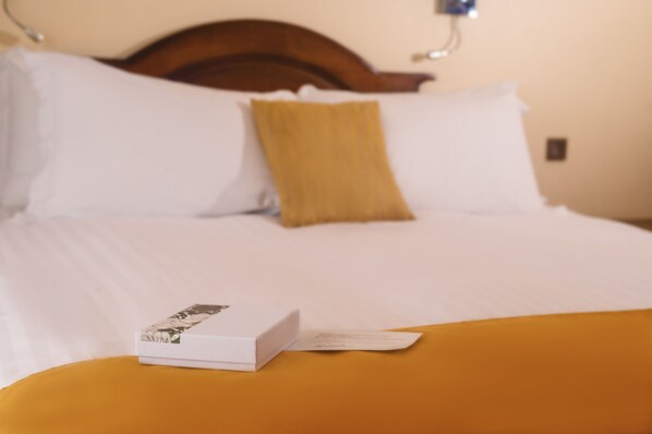 A neatly made bed with white and mustard pillows, a wooden headboard, and a white box on the bed. - Hotel Bakoua Les Trois Ilets (Trois-Ilets)