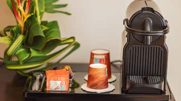 En kaffemaskin med en uppsamlingsbricka, en kaffekopp och ett paket kaffekapslar på ett träbord.