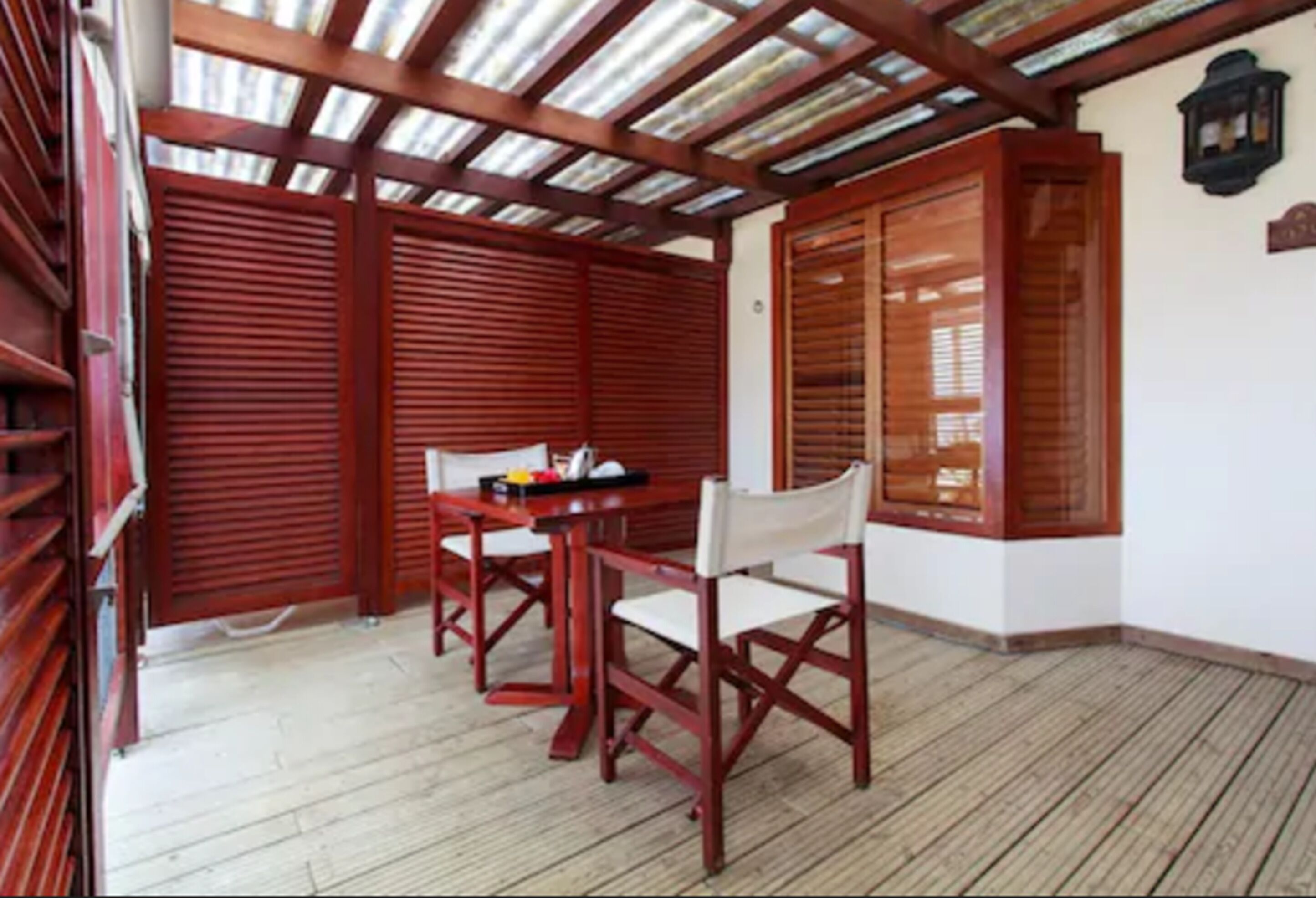 A covered outdoor area with a wooden table and chairs, a tiled floor, and a wooden door.