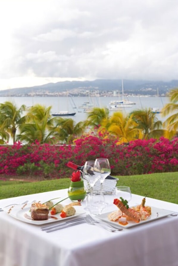 A table set for a meal with a view of the sea and boats in the background. - Hotel Bakoua Les Trois Ilets (Trois-Ilets)