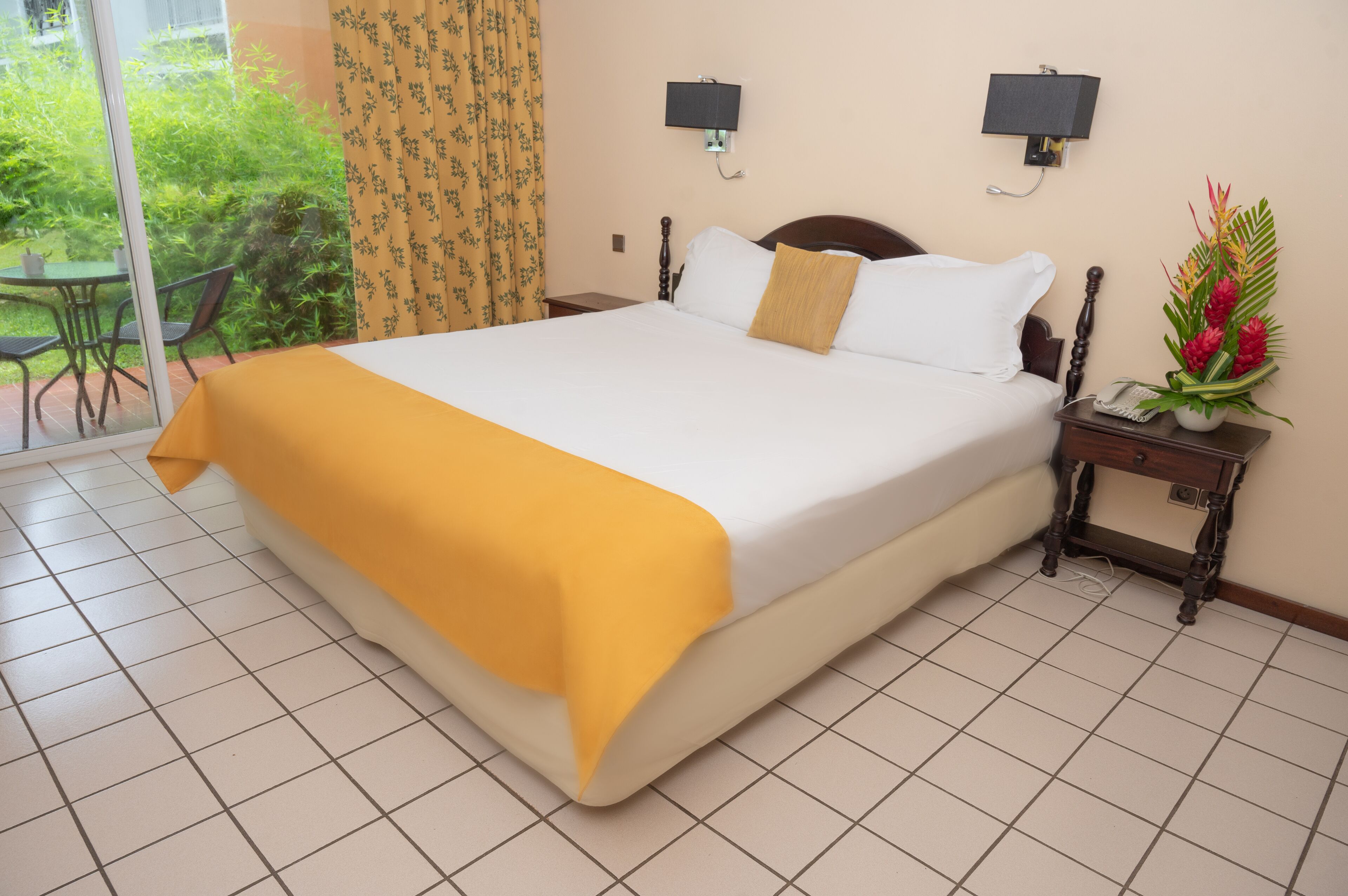 Une chambre d’hôtel avec un grand lit, une table de chevet avec une lampe et une vue sur le jardin, accessible par une porte coulissante.