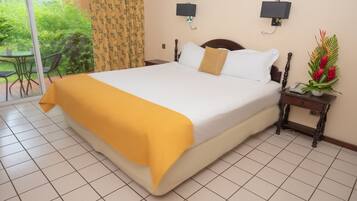 Una habitación de hotel con una cama grande, una mesita de noche con una lámpara y vistas al jardín a través de una puerta corredera.