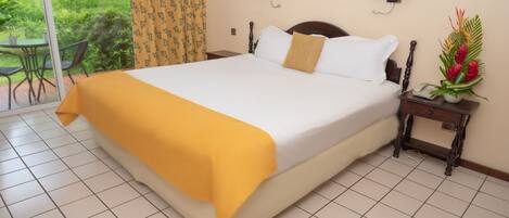 Una habitación de hotel con una cama grande, una mesita de noche con una lámpara y vistas al jardín a través de una puerta corredera.