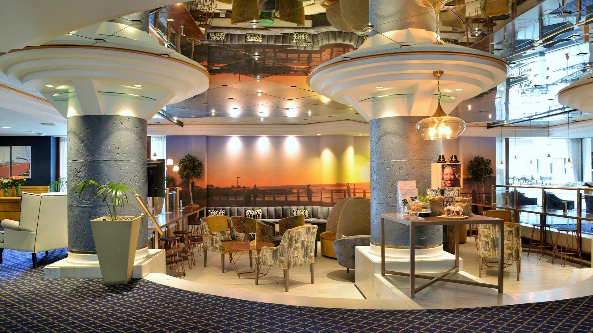 A spacious lobby with high ceilings, large pillars, and a seating area with tables and chairs.