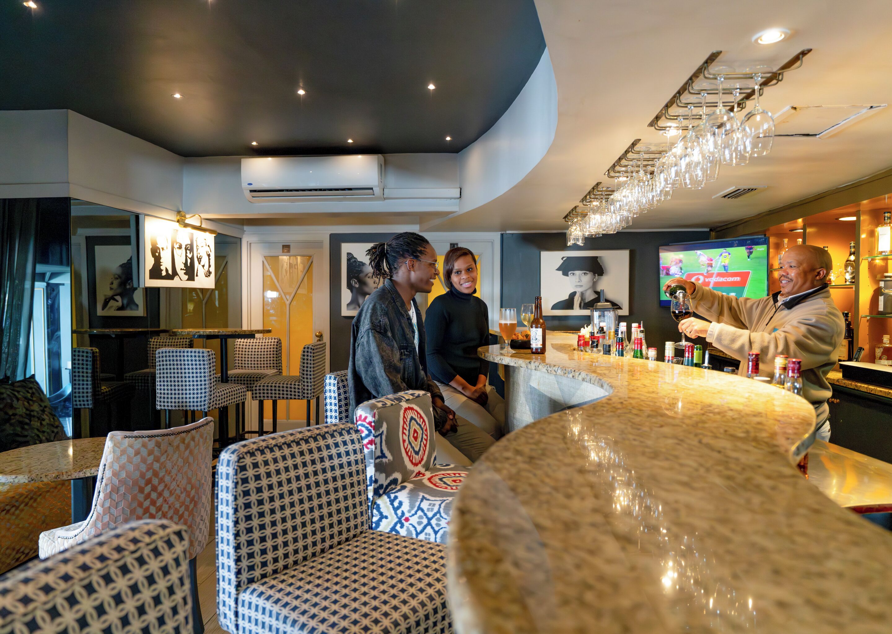 A bar area with a curved counter, patterned chairs, and a television screen.