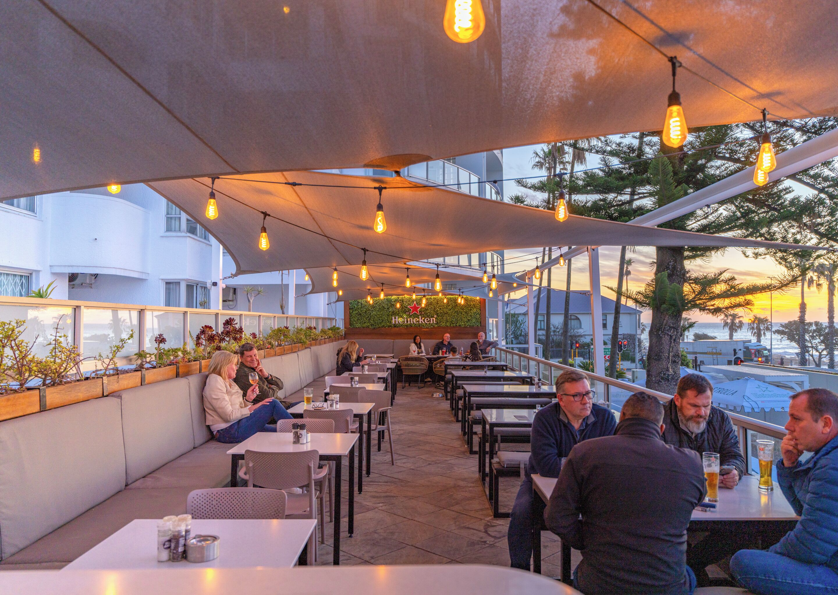 Un restaurant en plein air avec des tables et des chaises, une enseigne Heineken et une vue sur l’océan.