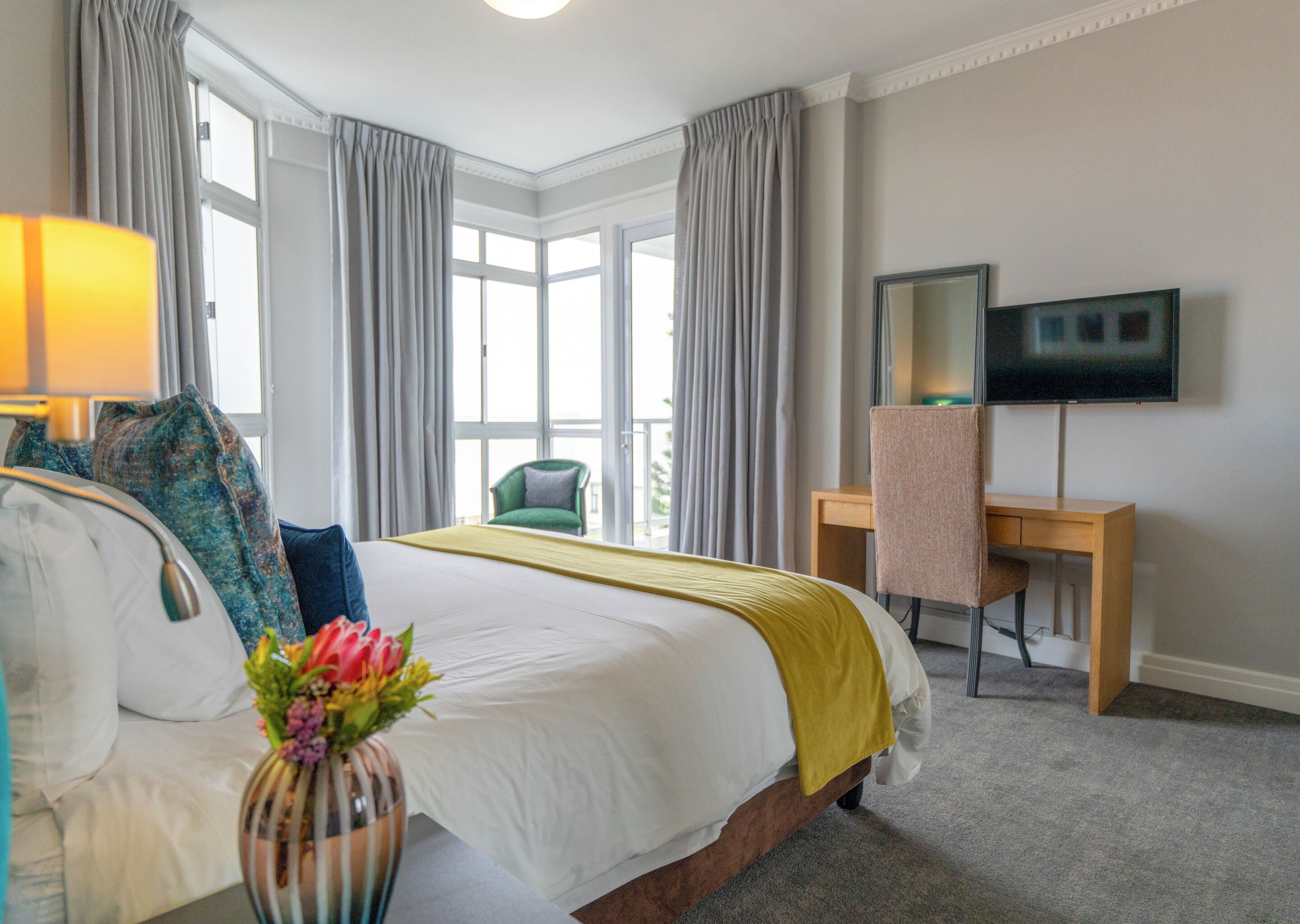 A hotel room with a bed, a desk, a chair, a TV, and a window with curtains.