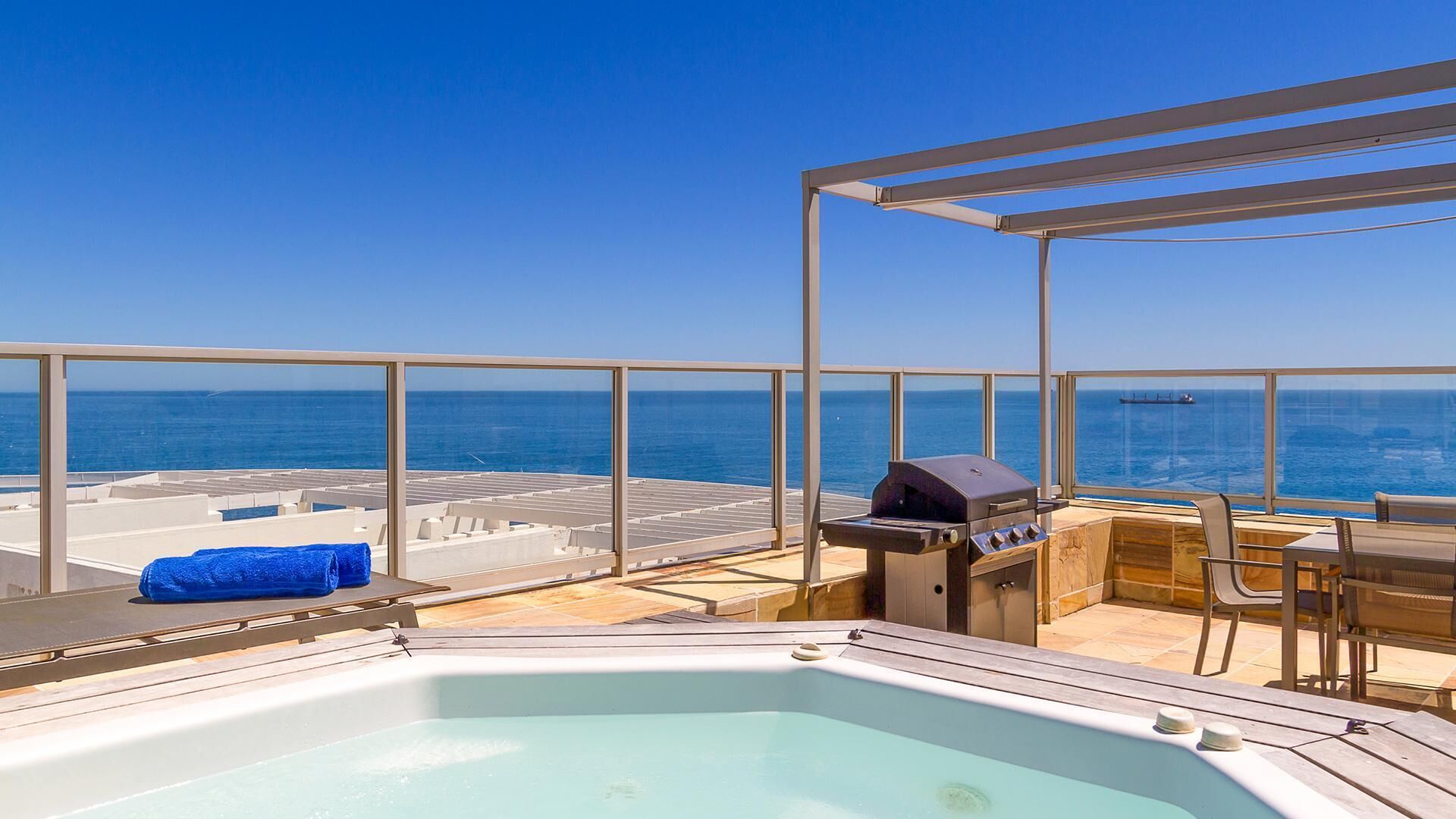A rooftop terrace with a hot tub, a grill, and a view of the ocean.