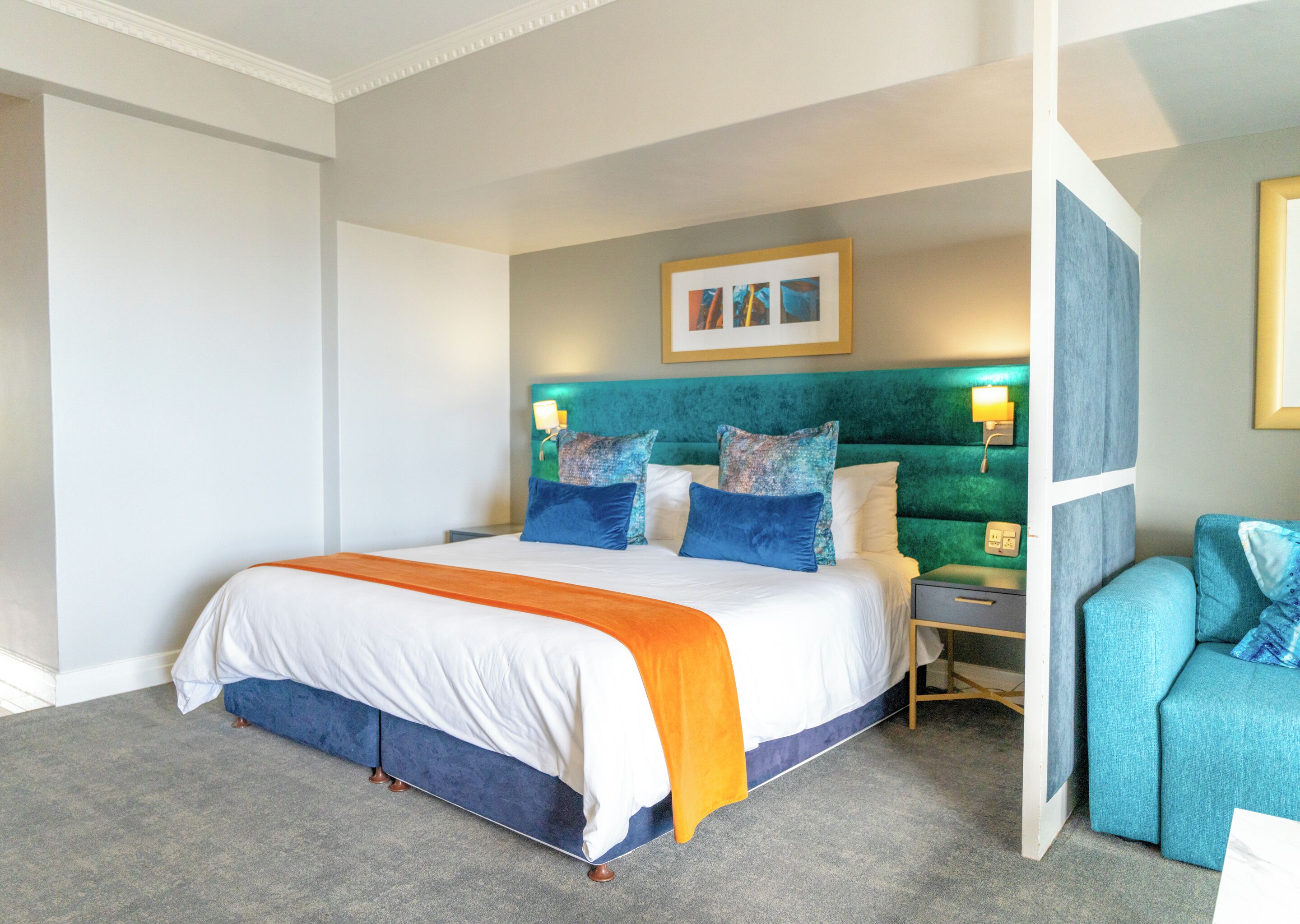 Ein Hotelzimmer mit einem großen Bett, einem Nachttisch, einem Sessel und einem Wandbild.