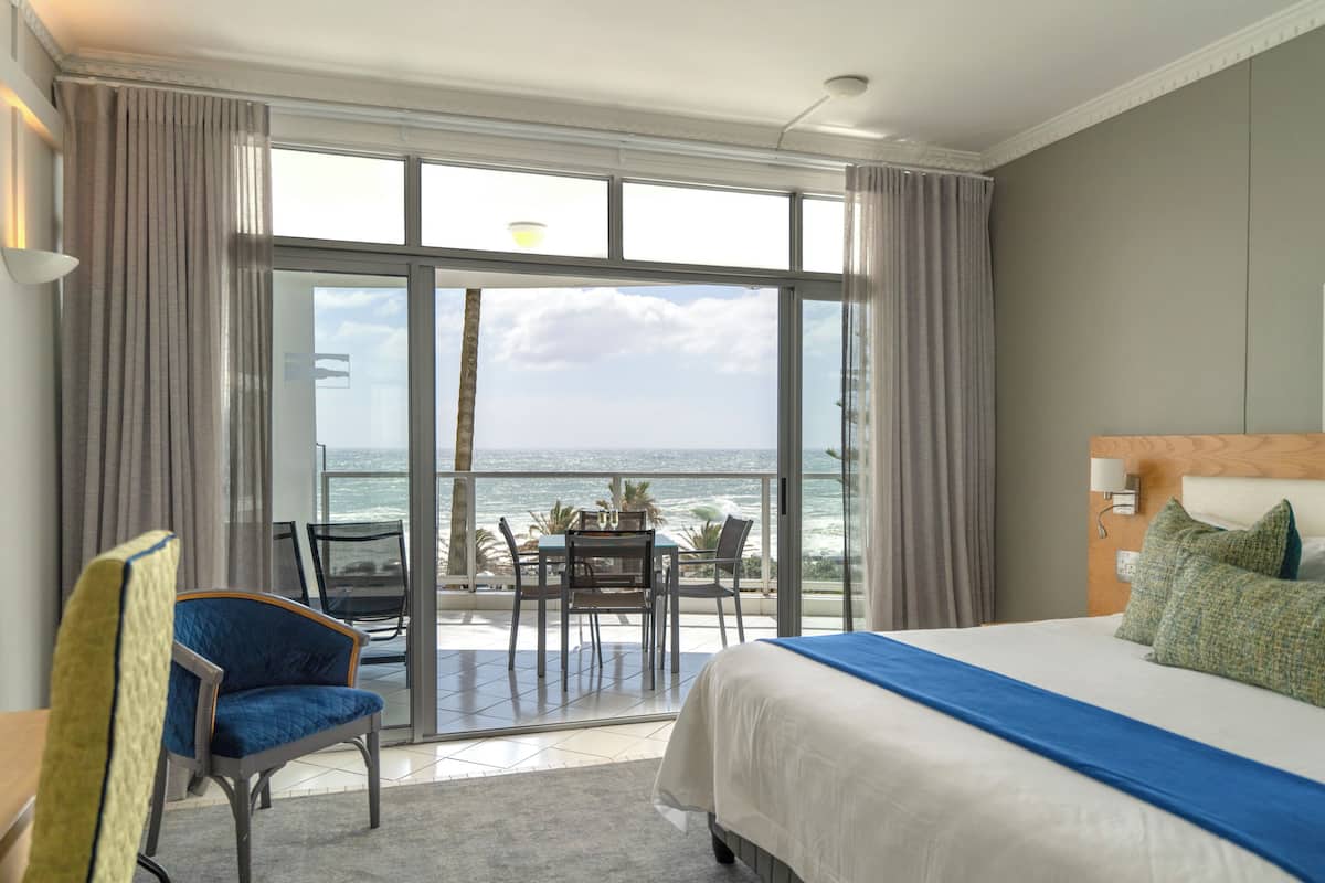 A hotel room with a bed, a chair, a table, and a view of the ocean.