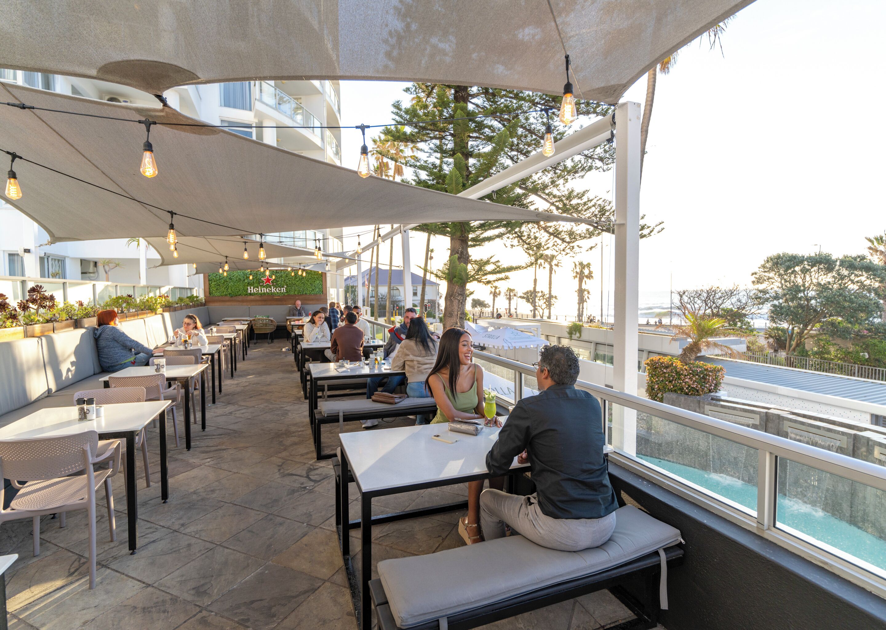 An outdoor dining area with tables and benches, a Heineken sign, and a view of the city.