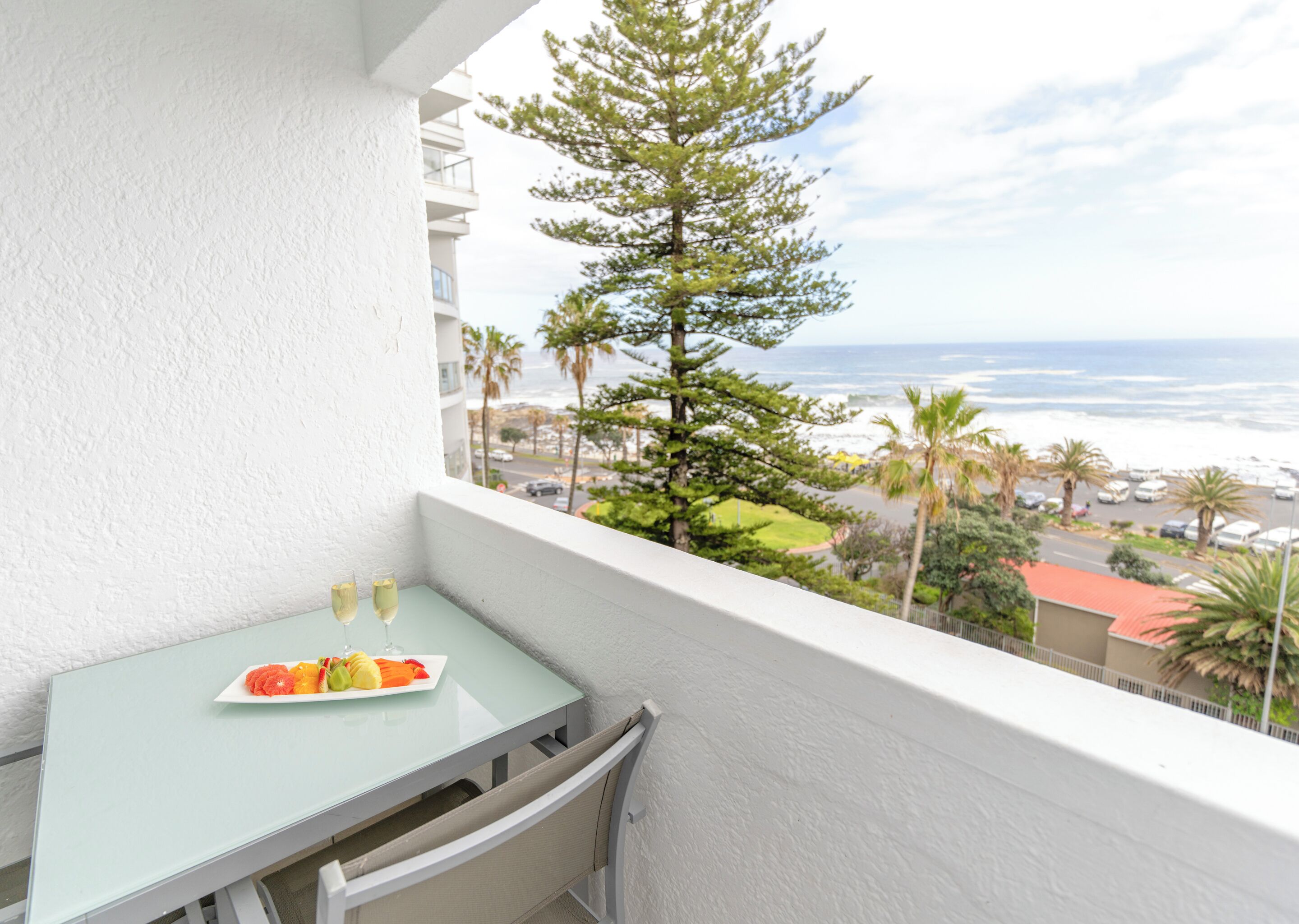 Een balkon met een tafel, twee glaasjes en een schaal fruit.