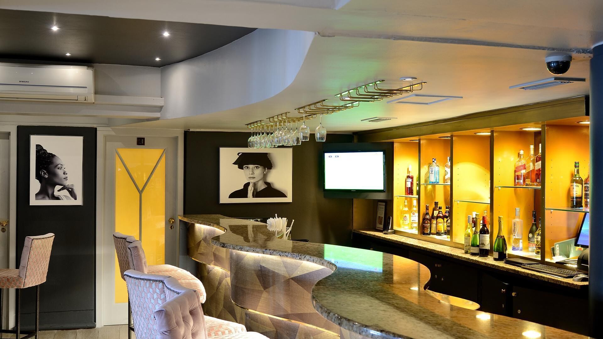 A modern bar area with a curved counter, a mounted television, and a selection of liquor bottles.