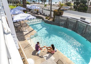 A swimming pool with a seating area, umbrellas, and a view of the beach.
