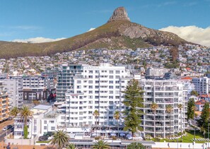 A coastal cityscape with a prominent mountain in the background, featuring a hotel with multiple floors and balconies.