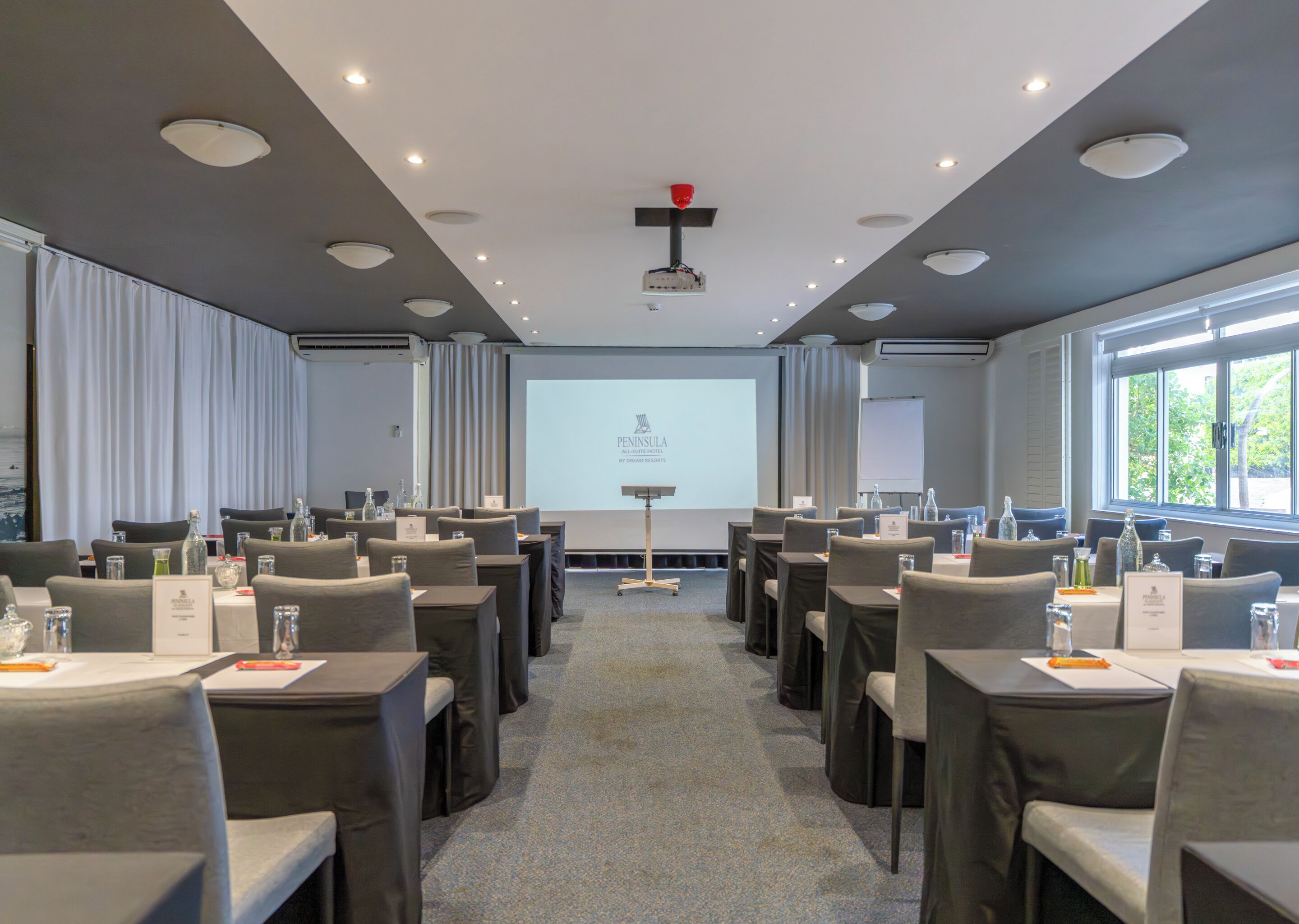 Ein Konferenzraum mit Tischen und Stühlen, einer Projektionsleinwand und einem Fenster mit Blick.