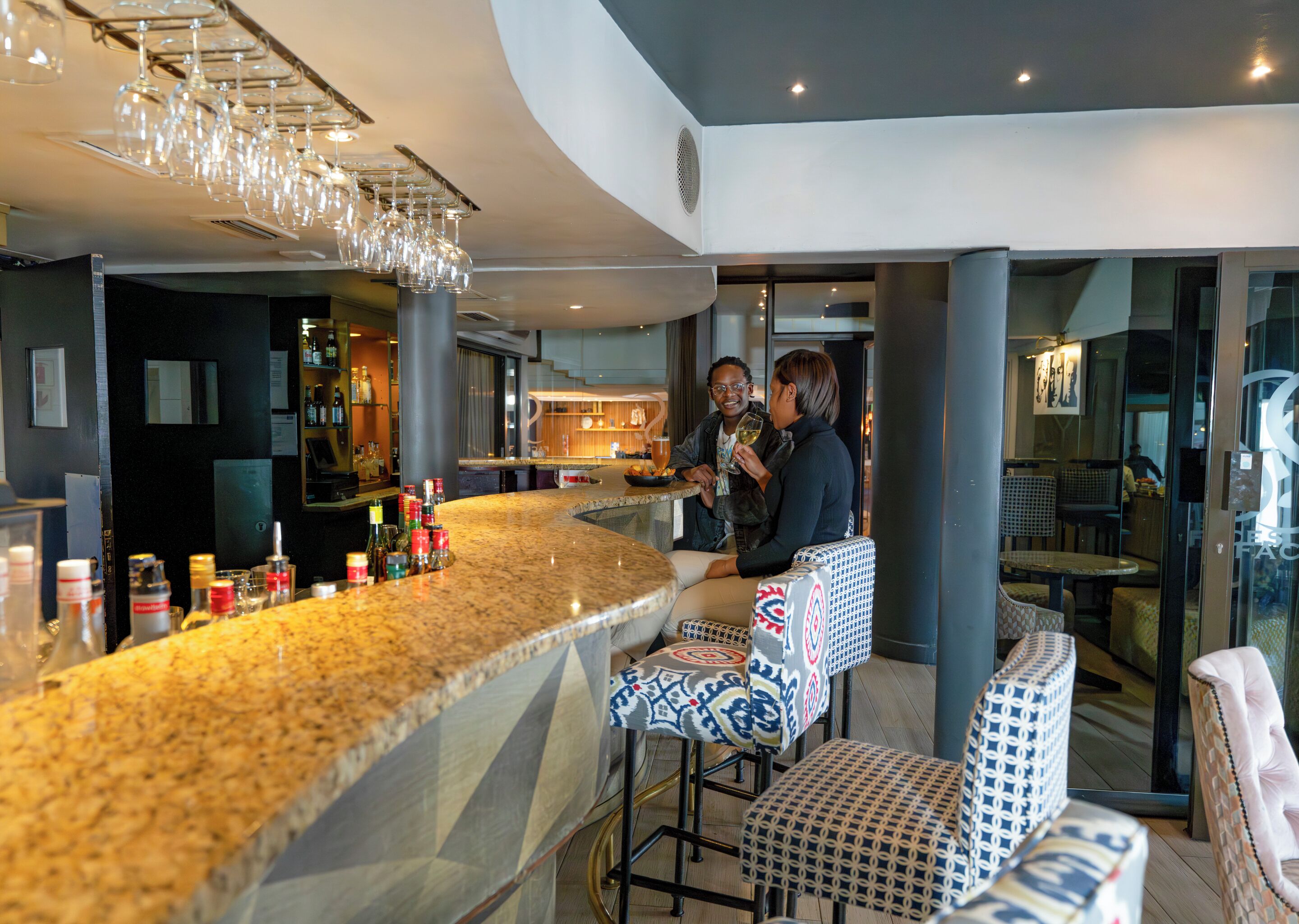 A bar area with a granite countertop, bar stools, and a hanging light fixture.