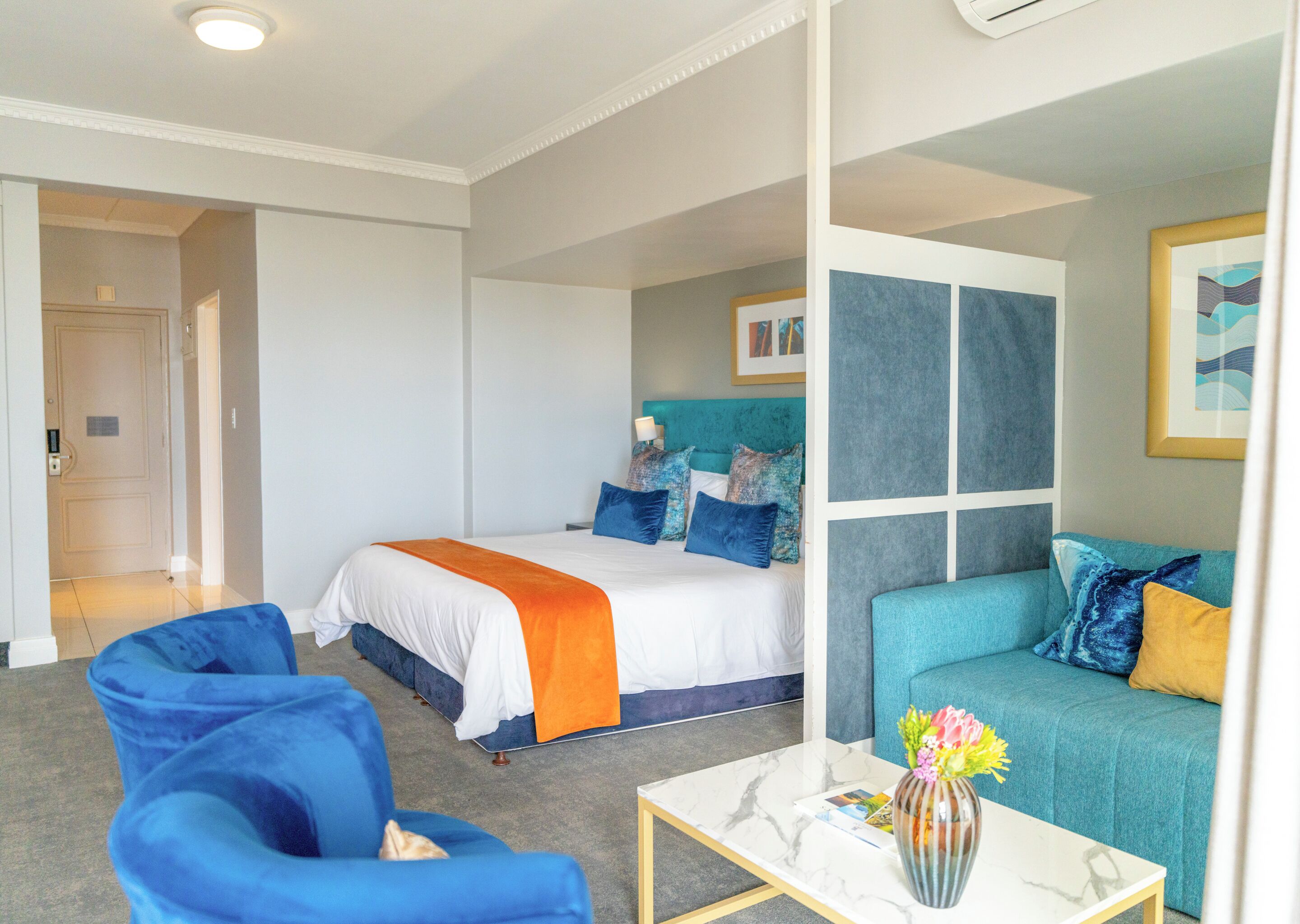 A hotel room with a bed, a sofa, a coffee table, and a door leading to another room.