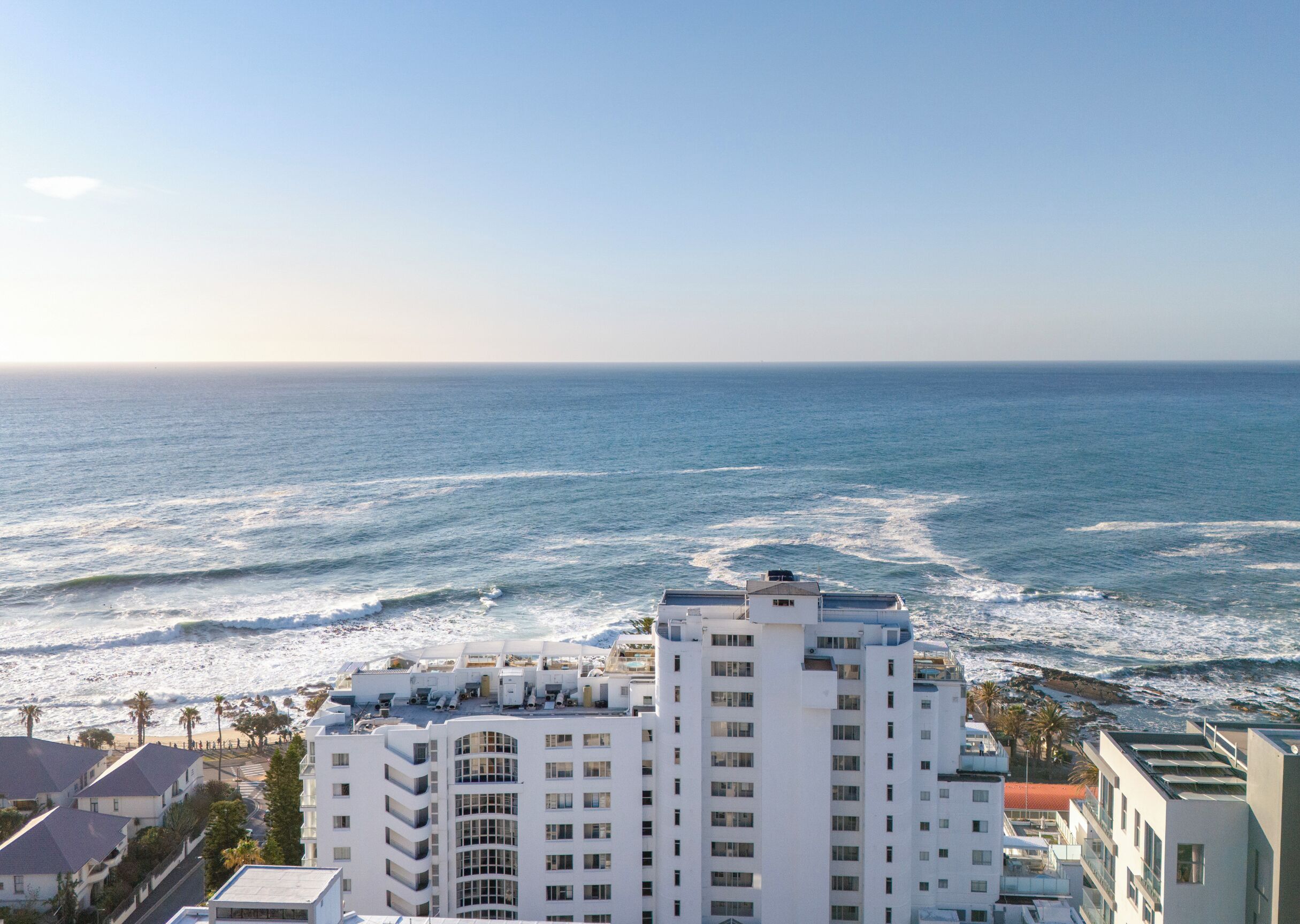 A coastal hotel with multiple floors, balconies, and a view of the ocean.