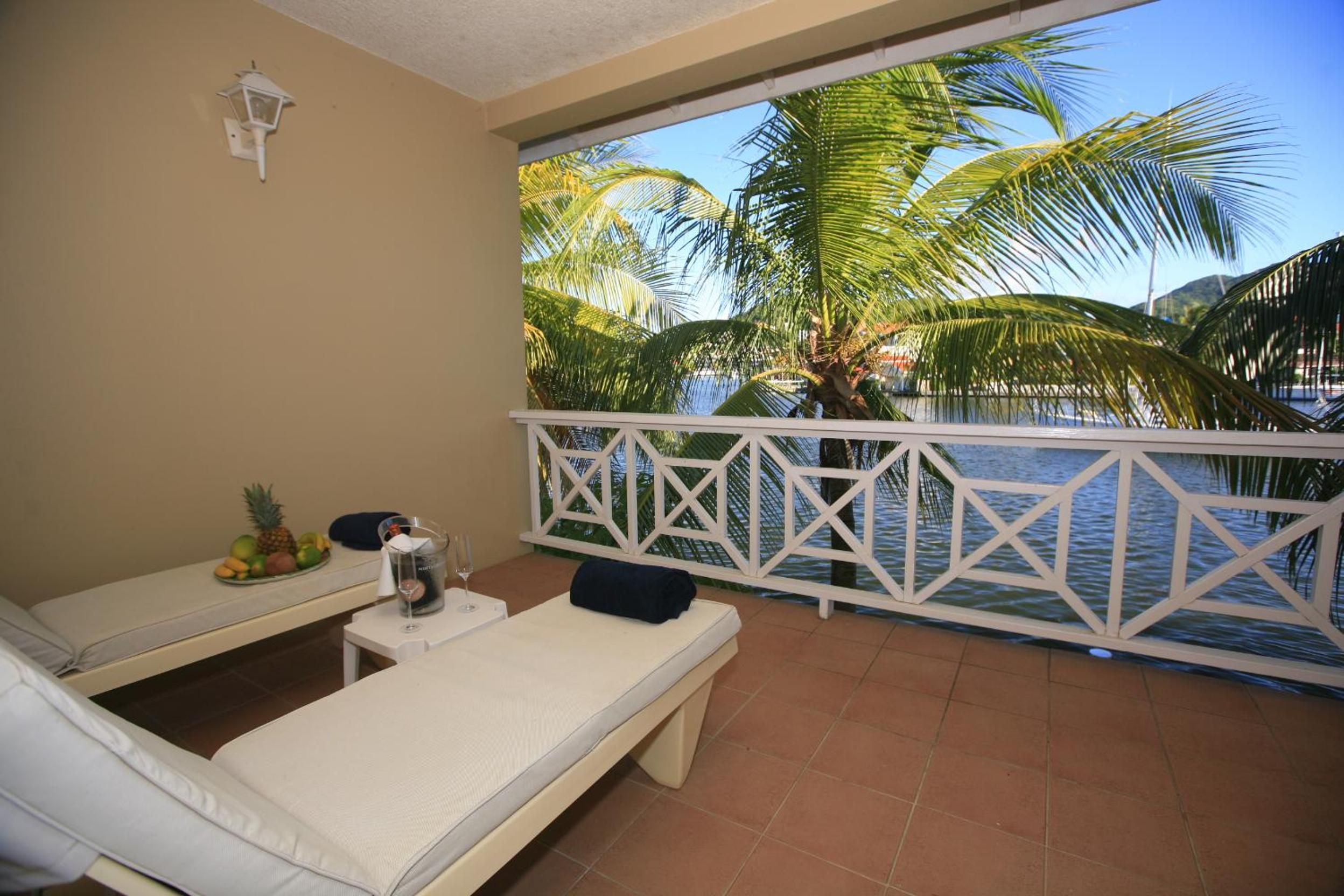 Un balcón con dos sillones, una mesita con una bebida y vista a palmeras y al agua.