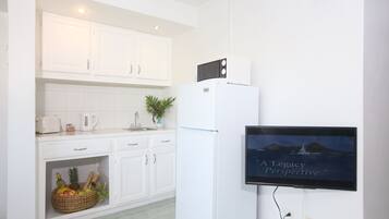 Cocina moderna con armarios blancos, microondas y refrigerador. Un televisor montado en la pared muestra el texto 'A Legacy Perspective'.