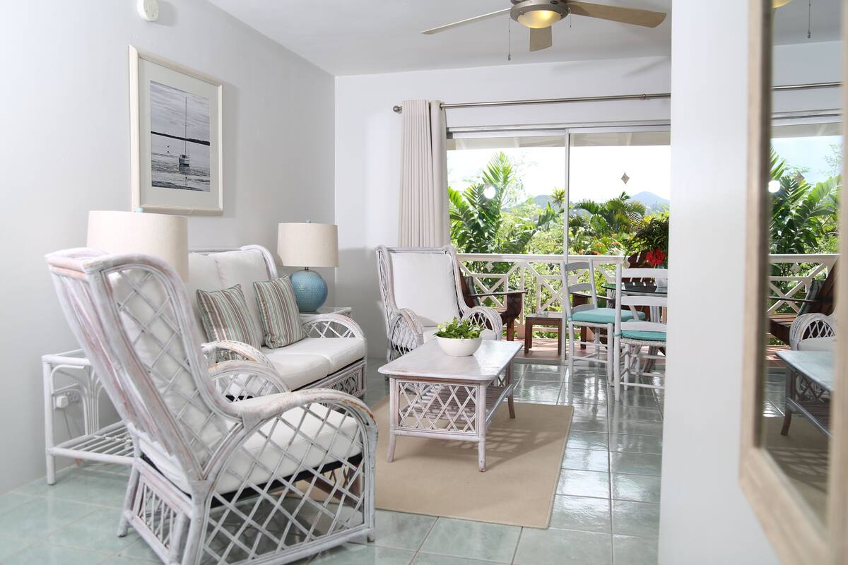 A room with wicker furniture, a ceiling fan, and a view of greenery outside.