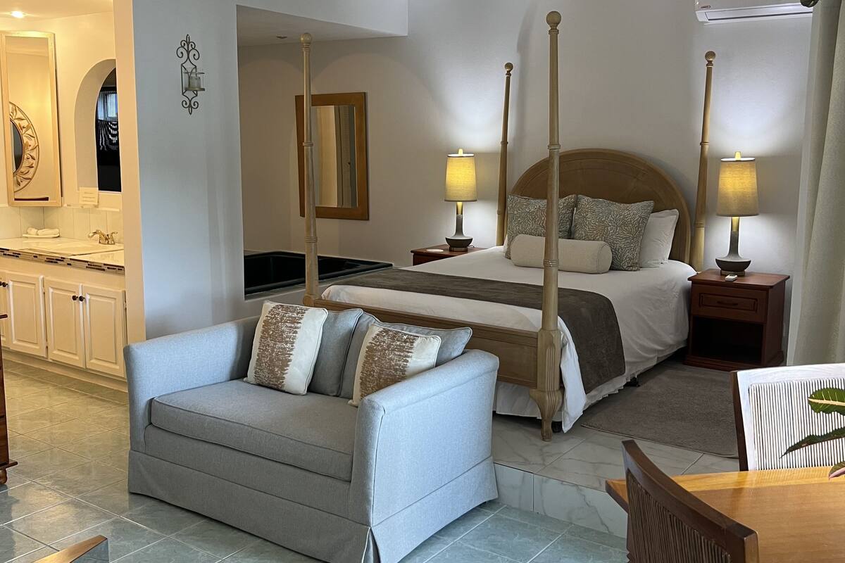 A hotel room with a bed, bedside tables, a sofa, a dining table, and a kitchen area.