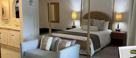 Una habitación de hotel con cama, mesitas de noche, sofá, mesa de comedor y zona de cocina.