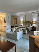Una habitación de hotel con cama, mesitas de noche, sofá, mesa de comedor y zona de cocina.