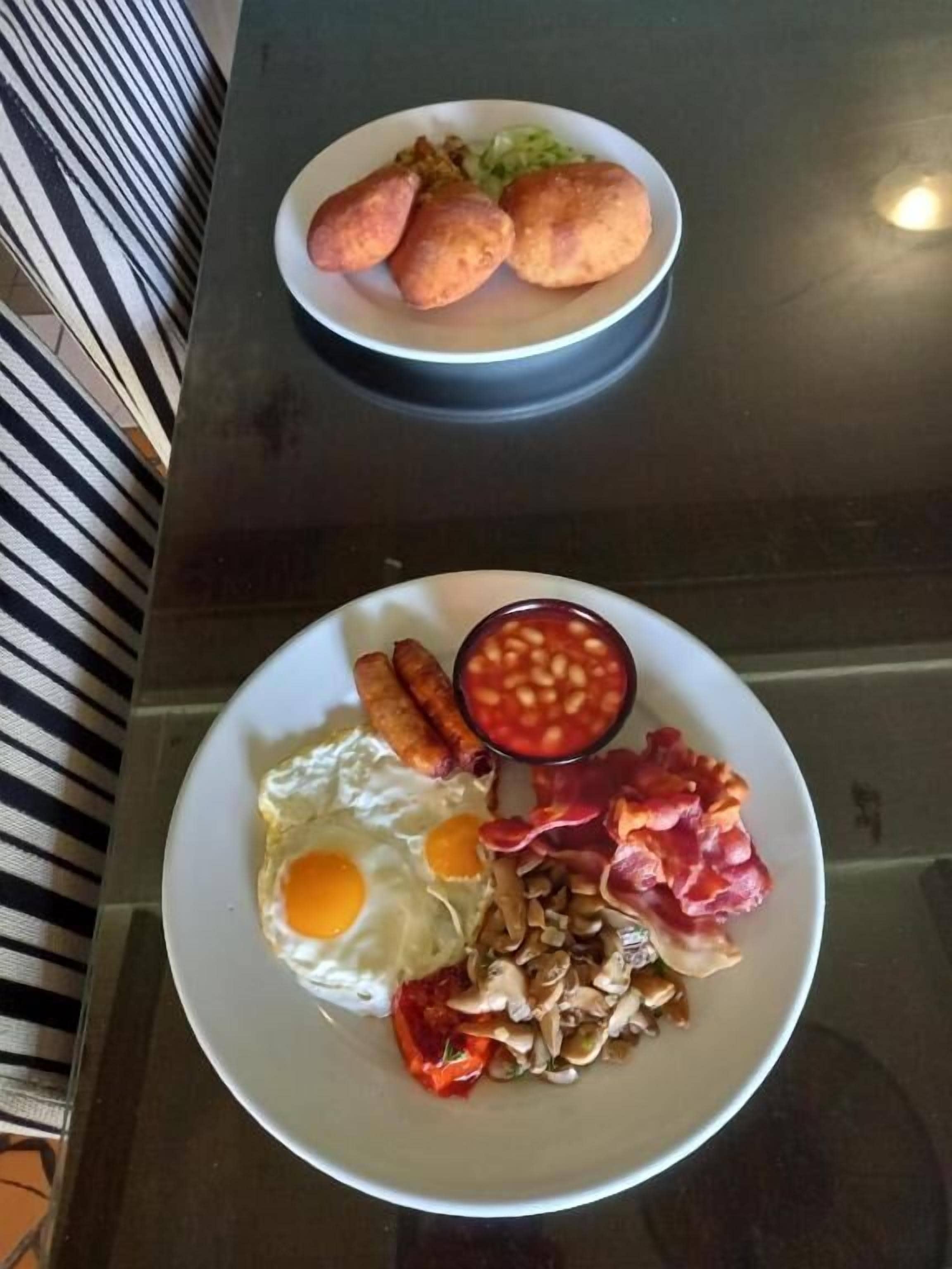 Una mesa con dos platos de comida, uno con huevos, salchichas, frijoles y tocino, y el otro con una ensalada y pan.